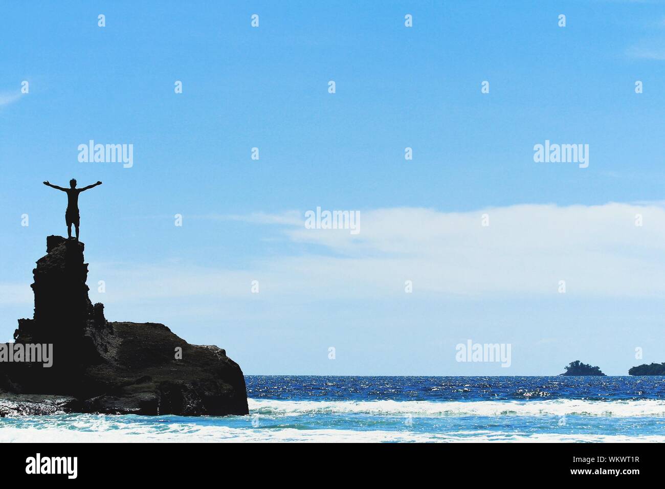 Man With Arms Outstretched On Cliff By The Sea Stock Photo