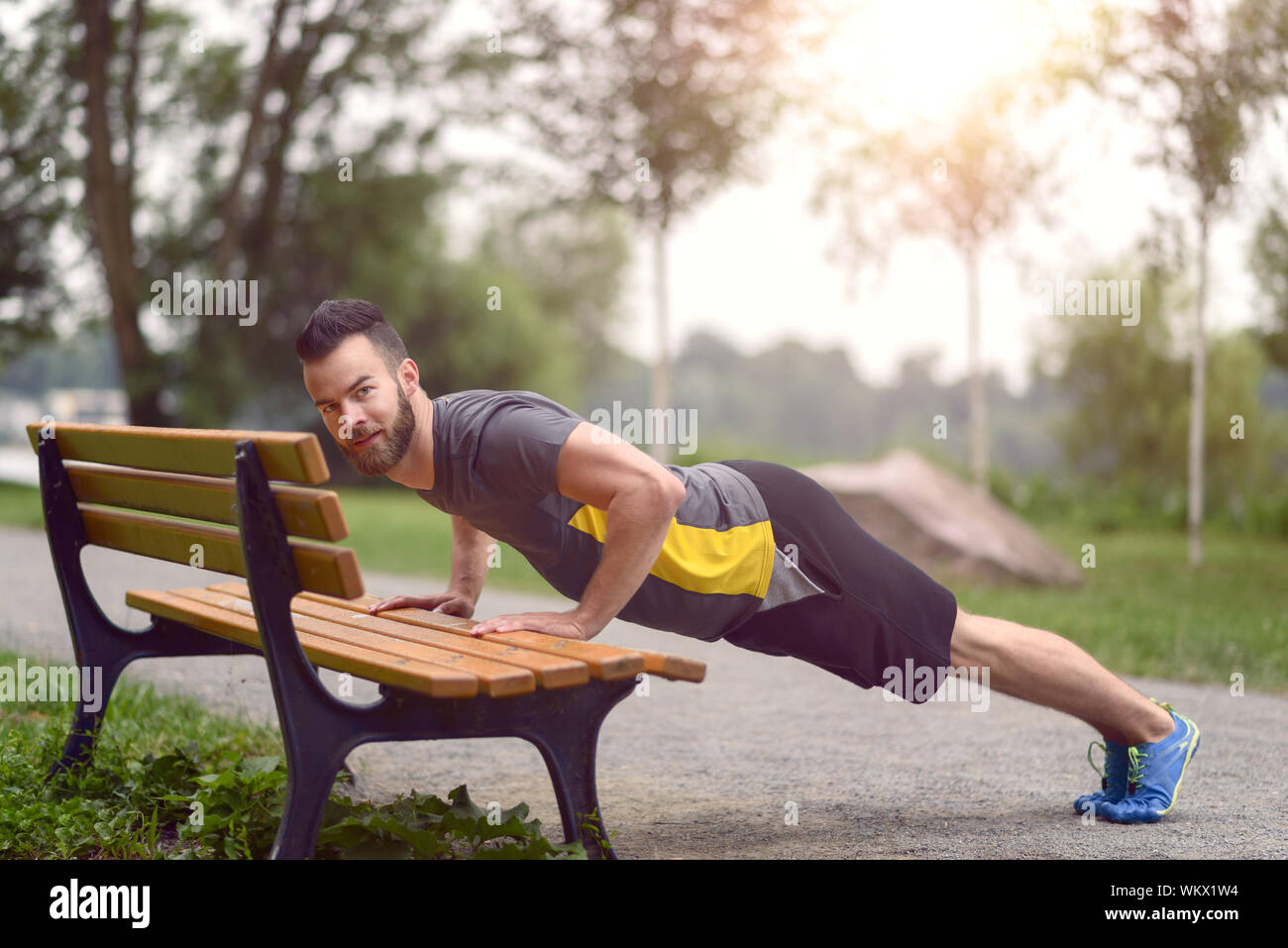 Portrait Of Smiling Man Doing Push Ups On Bench In Park Stock