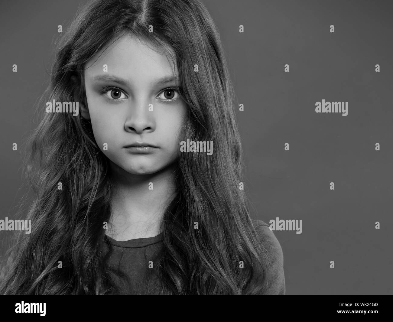 Thinking angry pupil kid girl with folded arms thinking and have an idea with finger under the face on grey studio background. Black and white. Closeu Stock Photo