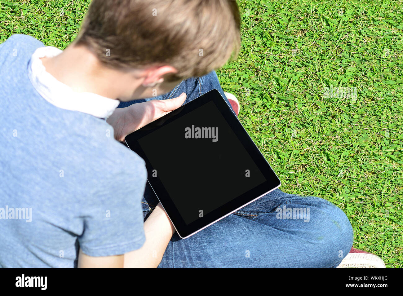 Boy sitting on lawn and using his new tablet pc Stock Photo