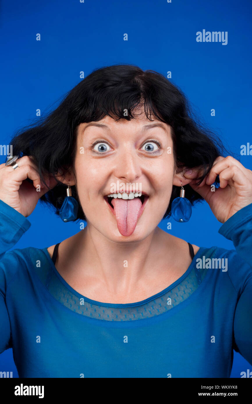 woman sticking out her tongue and pulling her ears isolated on blue