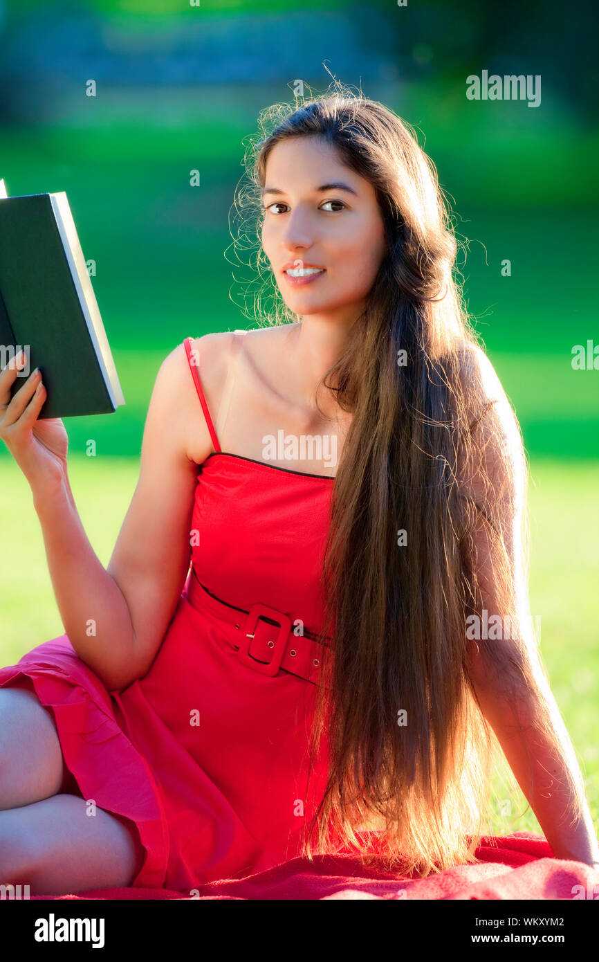 woman with long hair in red dress reading a book in a park Stock Photo ...