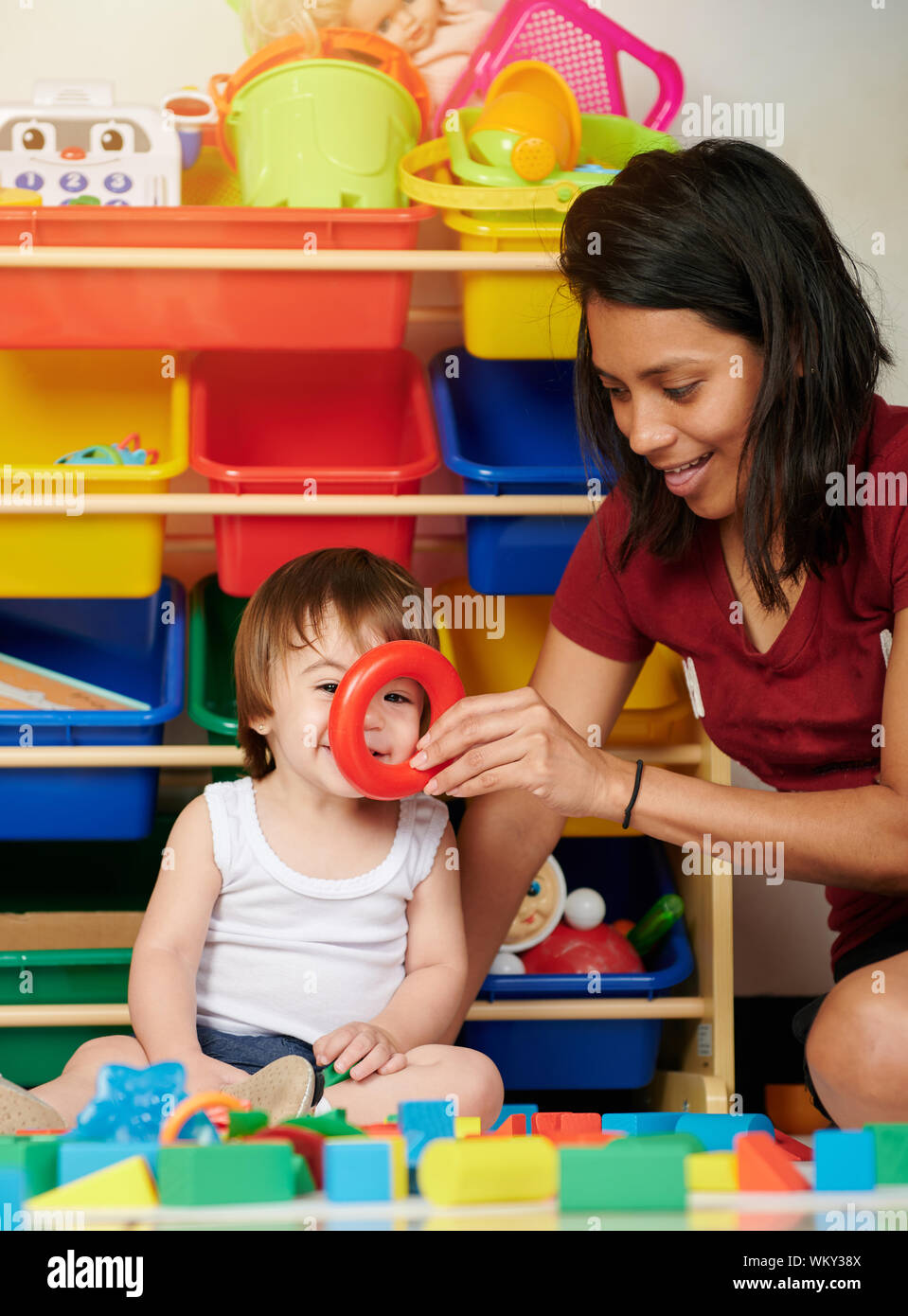 Babysitter have fun with baby on colorful toy background Stock Photo