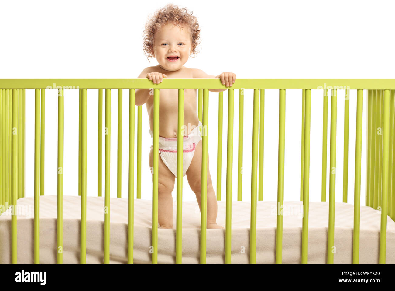 Smiling cute baby standing in a baby cot isolated on white background Stock Photo