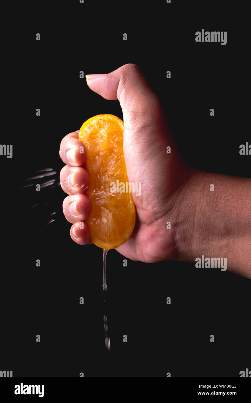 Cropped Hand Of Person Squeezing Orange Fruit Against Black Background Stock Photo