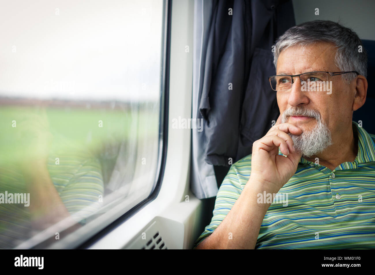 Senior man enjoying a train travel - leaving his car at home, he savours the time spent travelling, looks out of the window, has time to admire the la Stock Photo