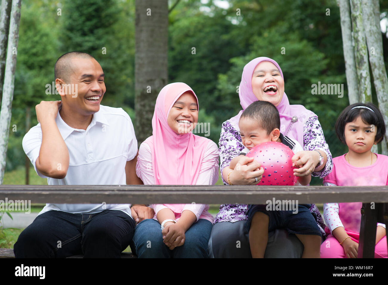 Happy Southeast Asian Family Sitting At Garden Bench Laughing