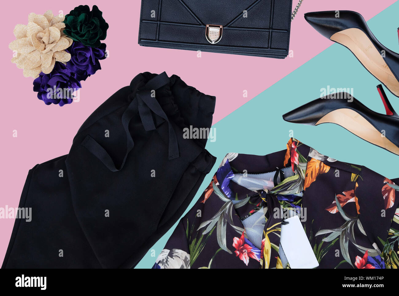 flat lay fashion set of black trausers, floreal shirt, black leather clutch bag, black hills and flower pins over pink and turquoise blue background Stock Photo
