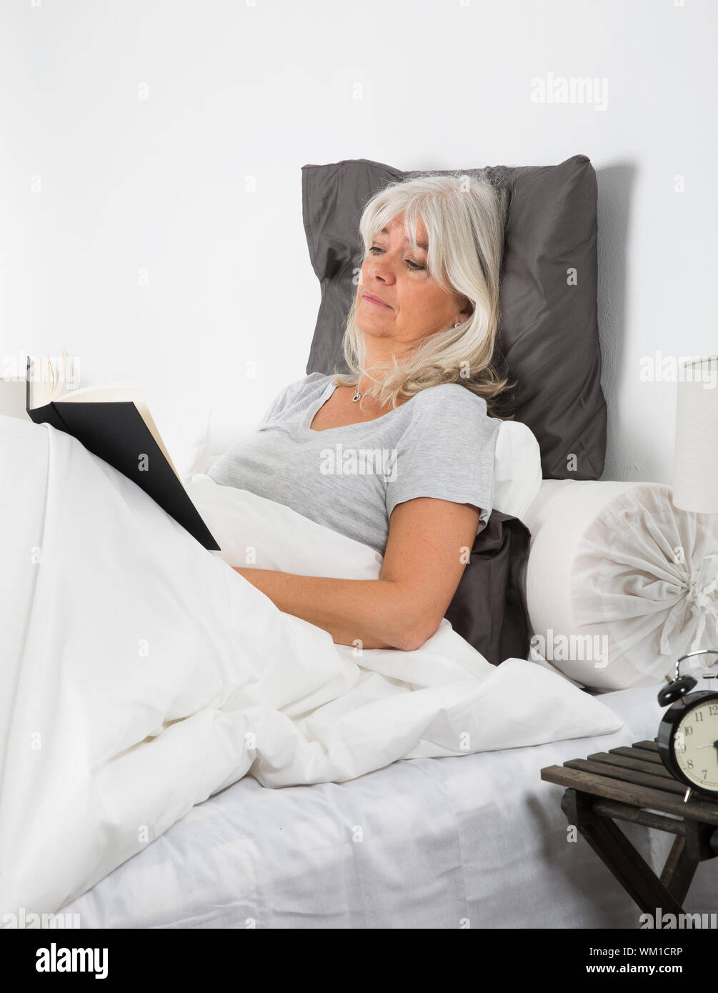 Tired woman reading a book in bed Stock Photo - Alamy