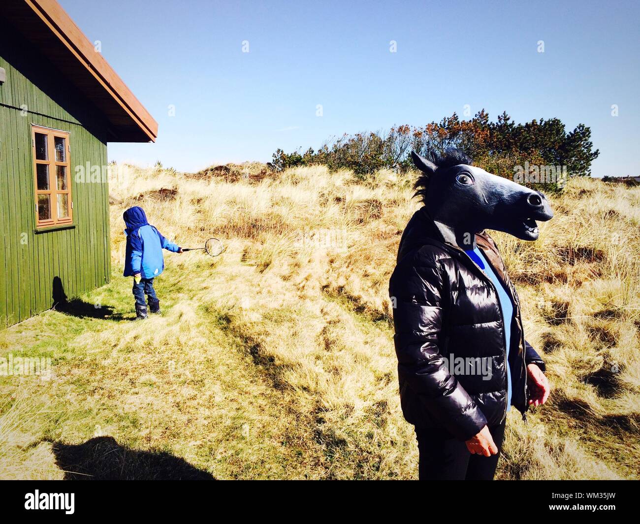 Woman Wearing Donkey Mask With Boy Playing By House Against Clear Sky Stock Photo