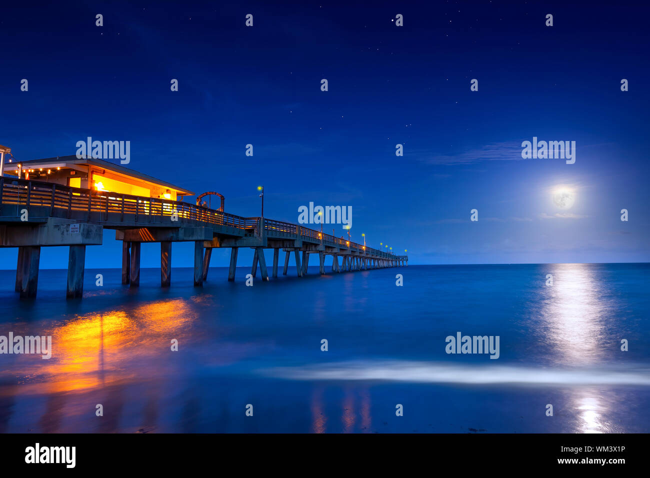 A beautiful full moon rises over the Atlantic Ocean at the Dania Beach Pier in Florida. The Dania Beach Pier is the perfect place to watch the moon. Stock Photo