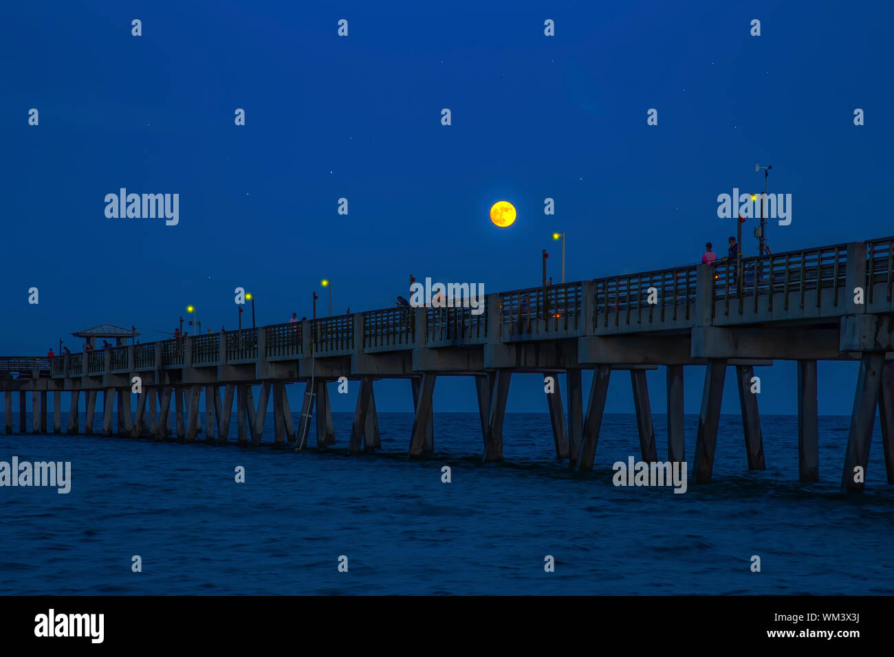 A full moon rises over the Dania Beach Pier in Florida as fisherman hope for a bite and tourists stroll the pier. Stock Photo