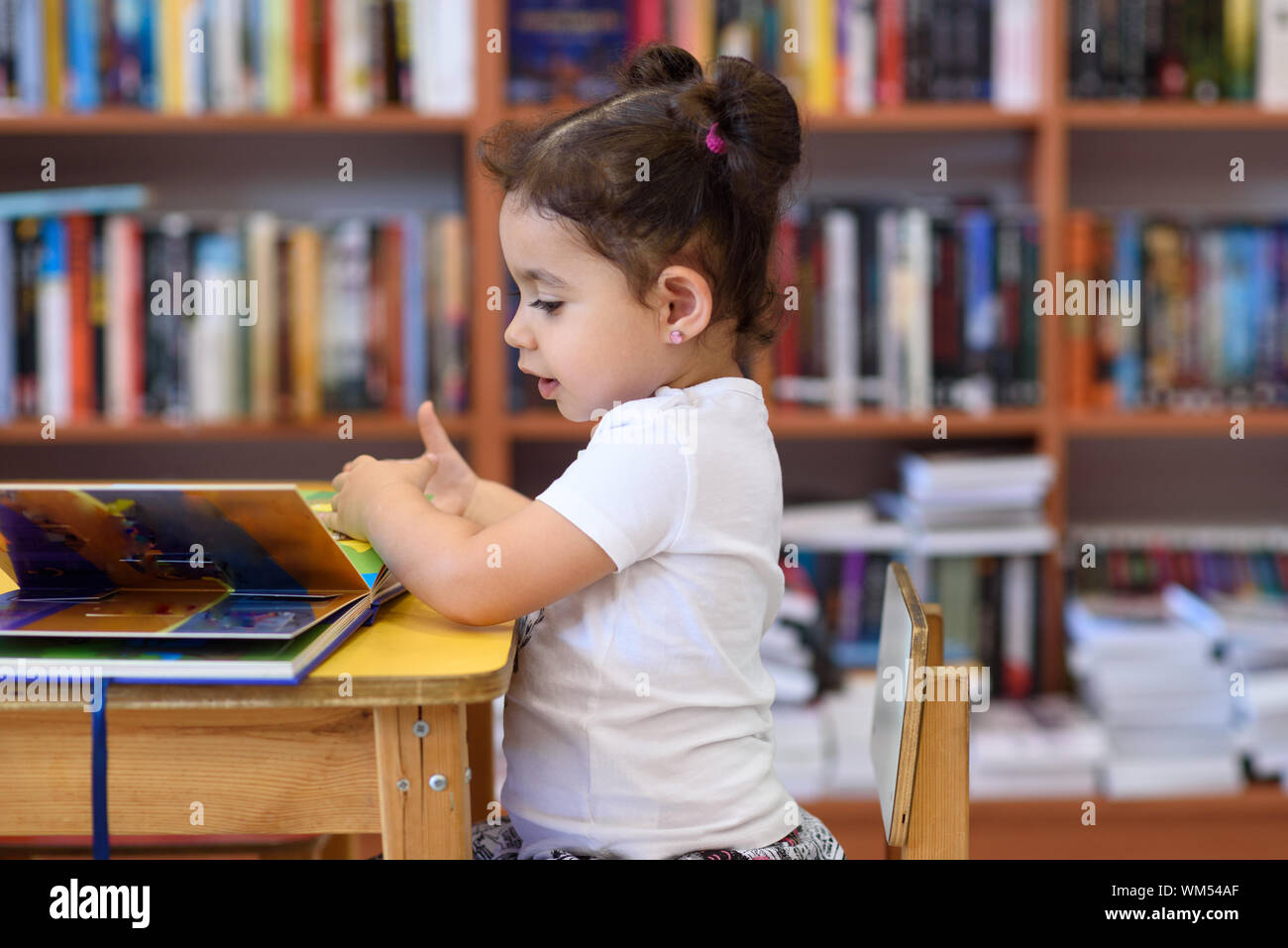 Little Girl Indoors In Front Of Books. Cute Young Toddler Sitting On A