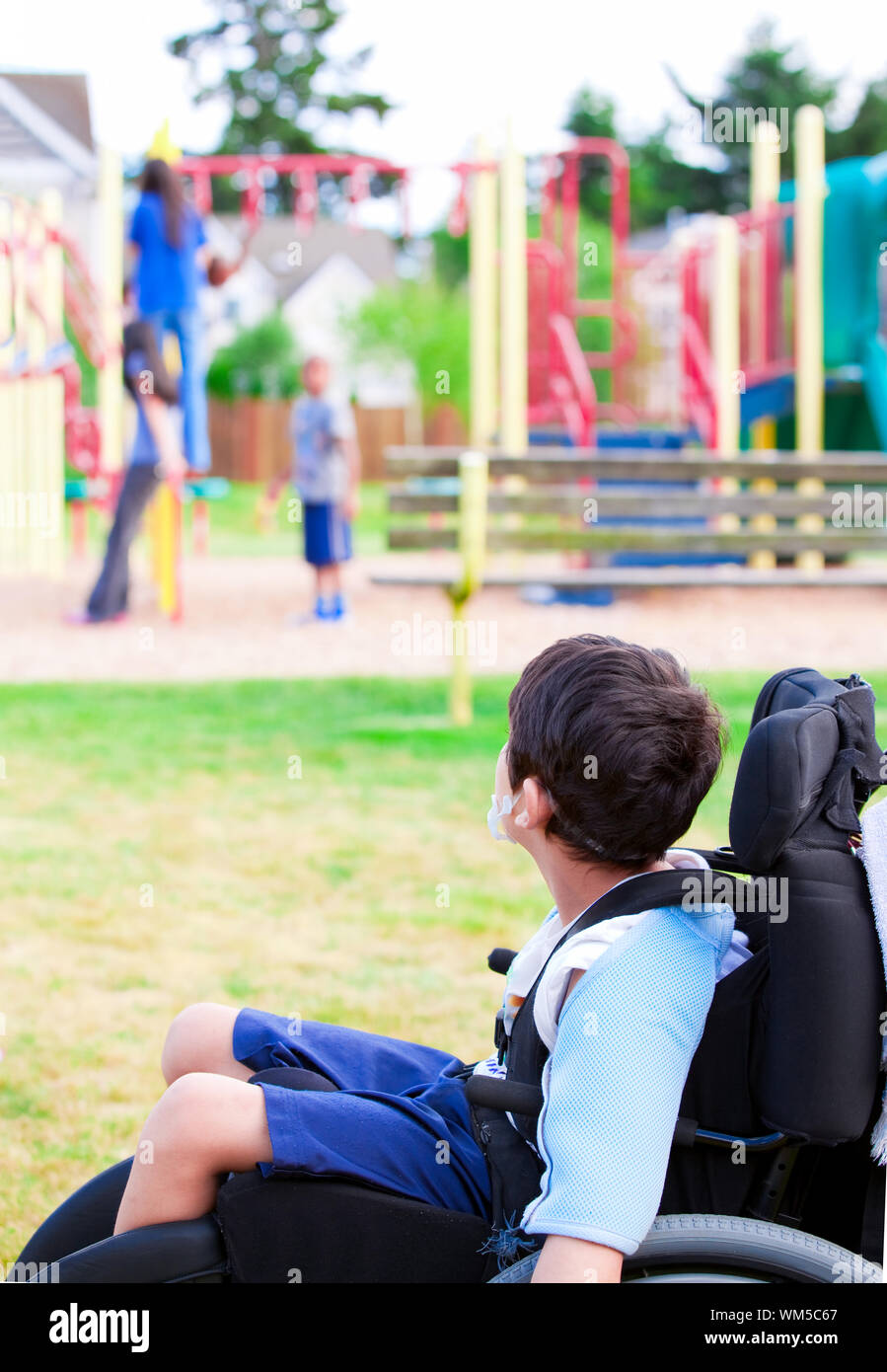 Disabled little boy in wheelchair watching children play on play Stock Photo