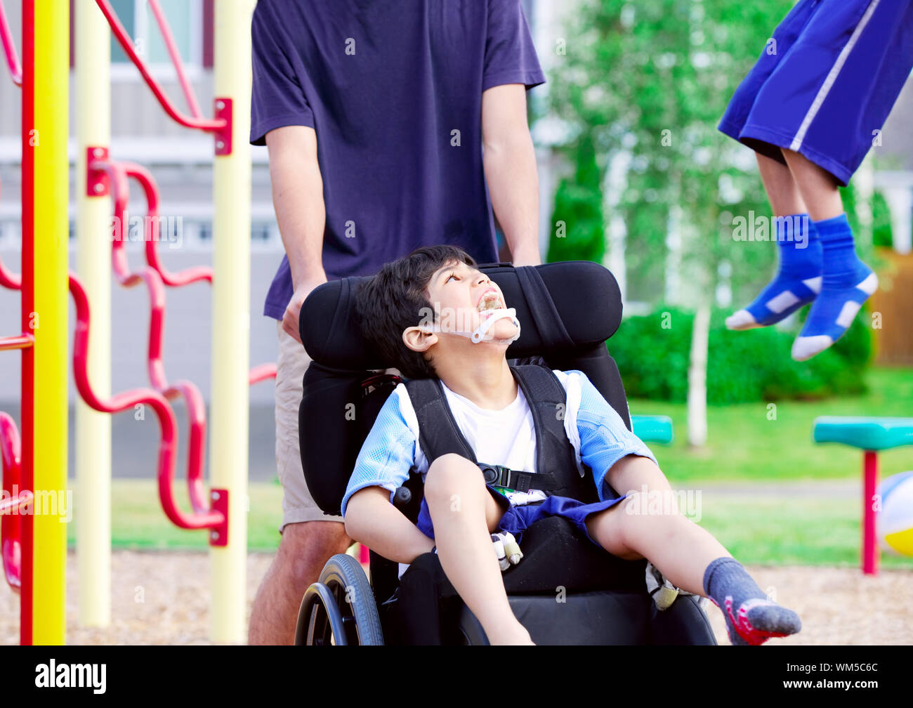 Disabled Boy In Wheelchair Enjoying Watching Friends Play At Park On ...