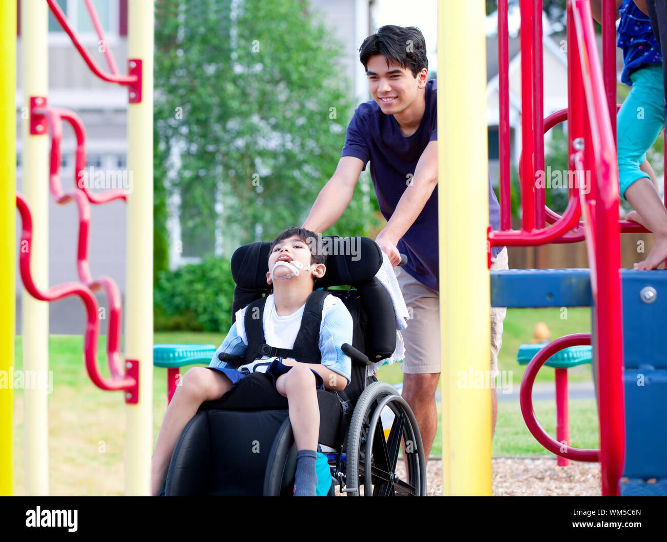 Disabled boy in wheelchair enjoying watching friends play at par Stock Photo