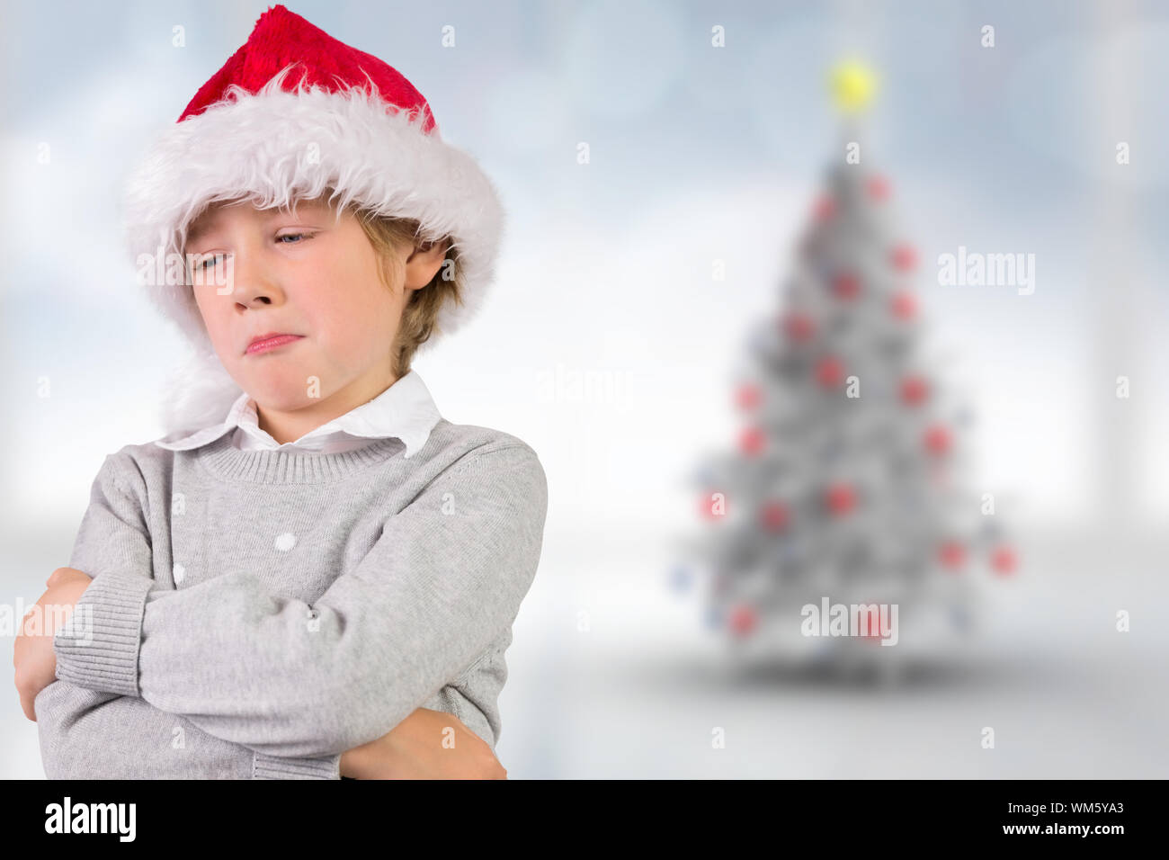 Festive boy sulking against blurry christmas tree in room Stock Photo