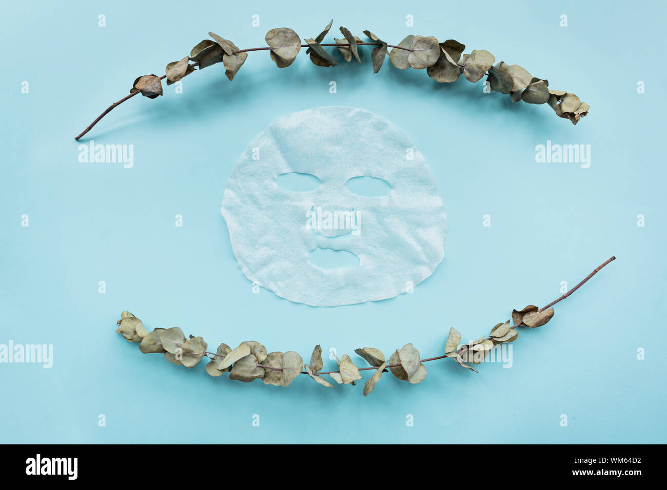 Sheet facial mask and eucalyptus branch on pastel blue paper background