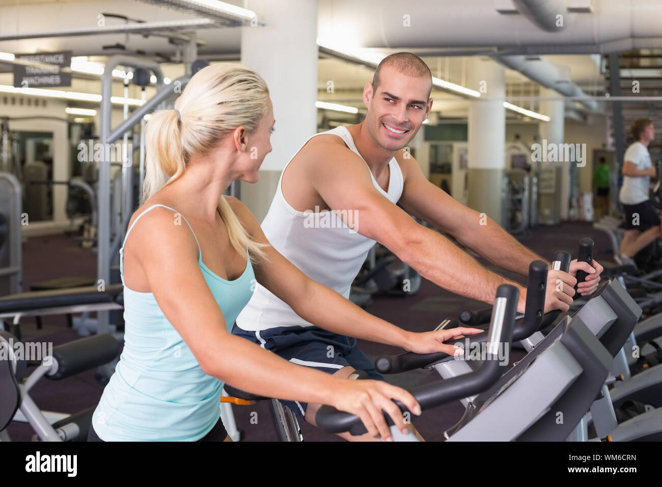 Side view of a fit young couple working on exercise bikes at the gym ...