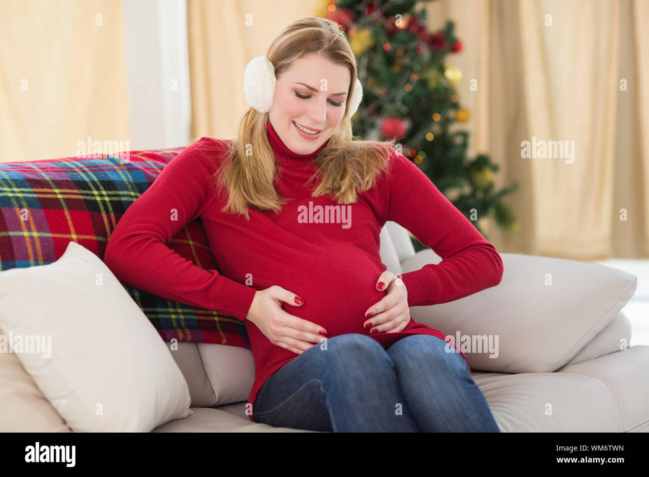 Beautiful pregnant woman holding her belly sitting on couch at home in the living room Stock Photo