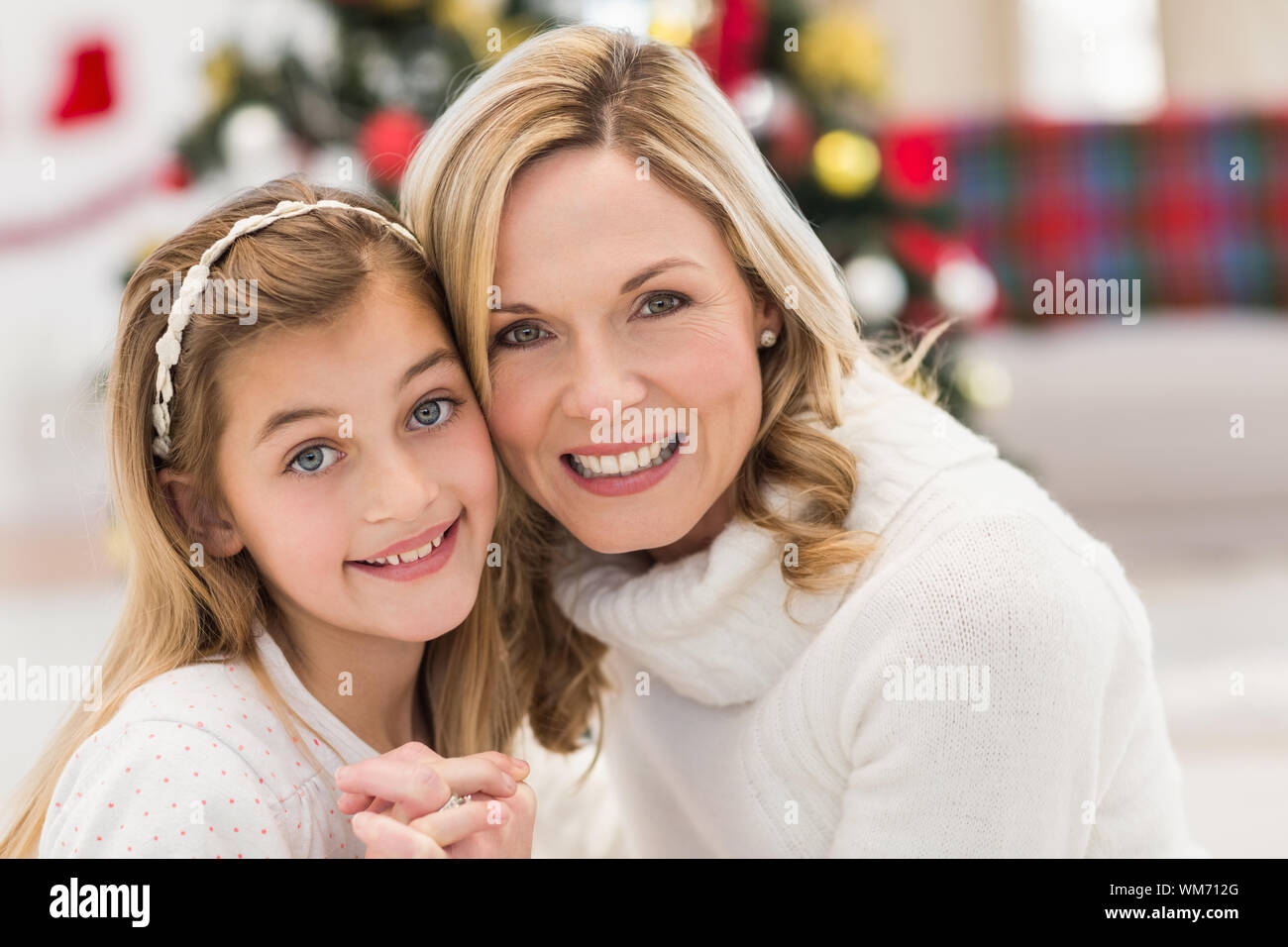 Festive mother and daughter beside christmas tree at home in the living room Stock Photo