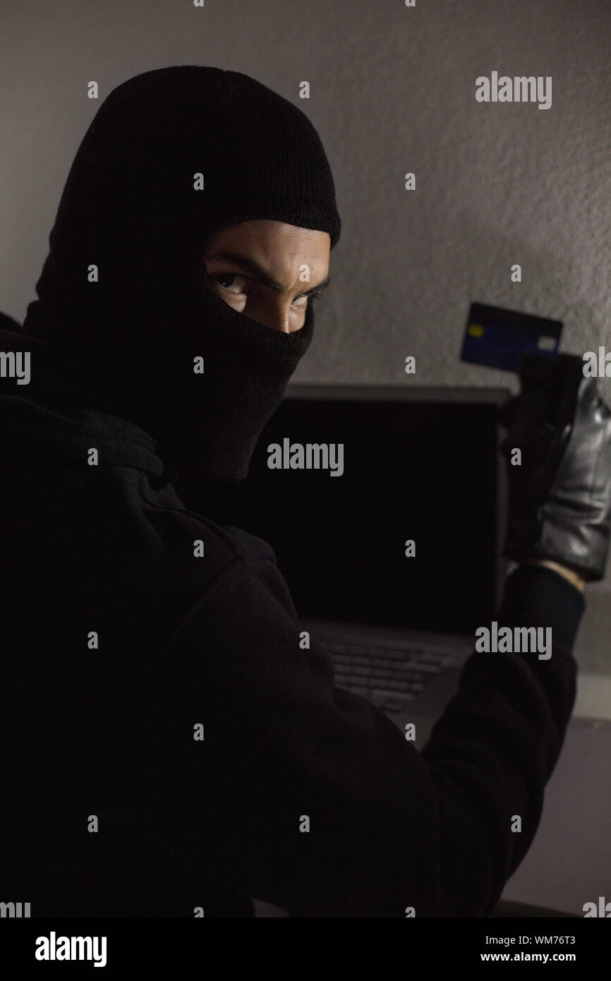 Hacker using debit card and laptop in house Stock Photo