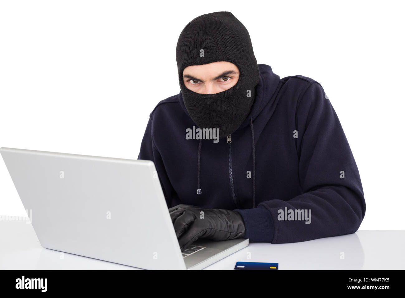 Hacker in balaclava hacking a laptop on white background Stock Photo