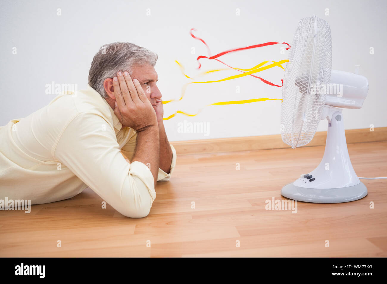 Man lying on floor looking at fan at home in the living room Stock