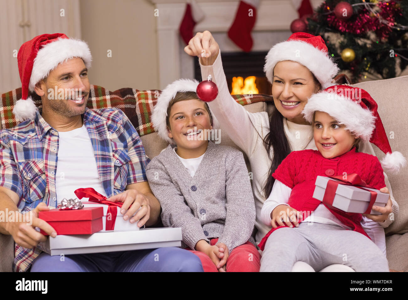 Festive family wearing santa hat on the couch at home in the living room Stock Photo
