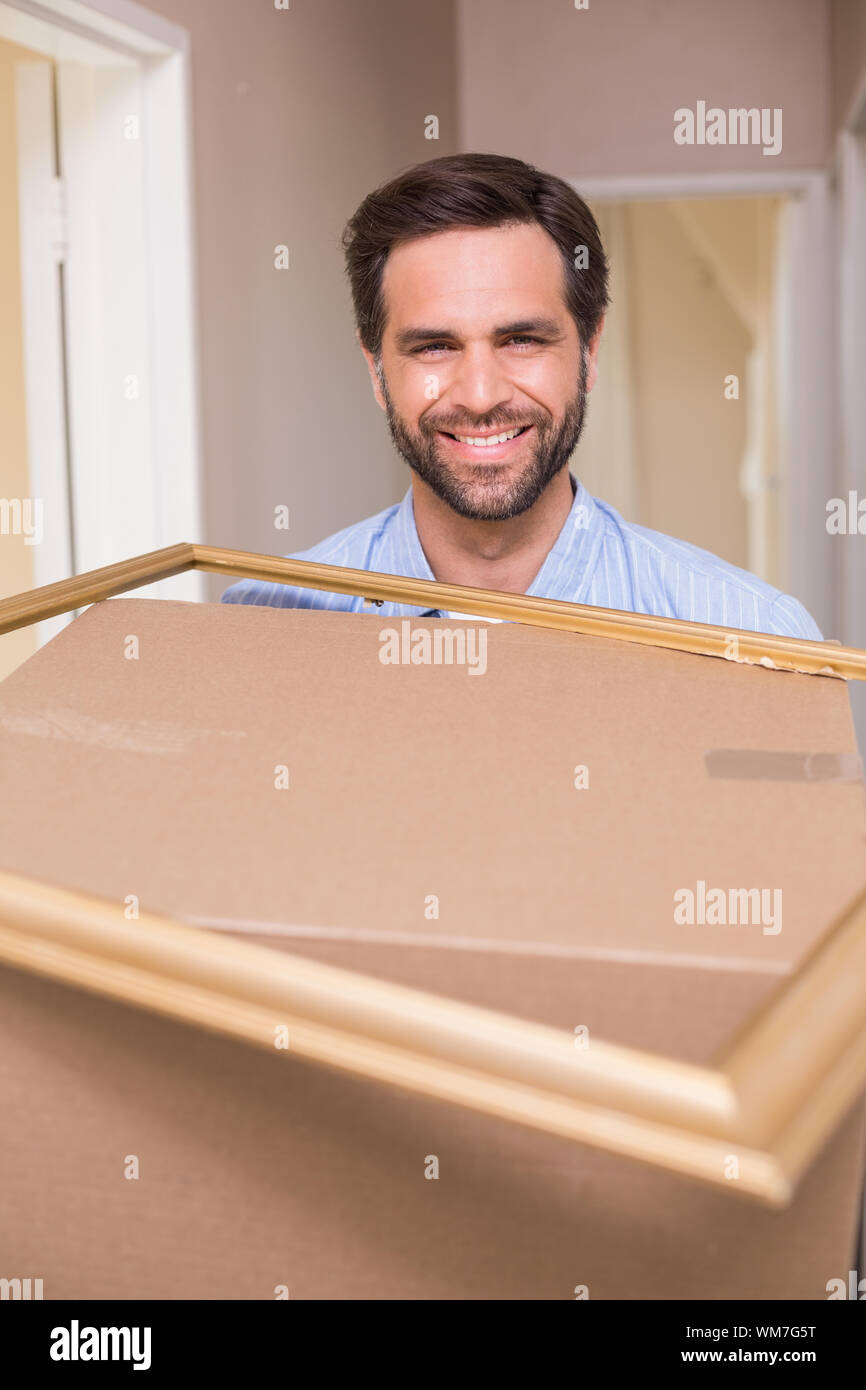 Happy man carrying moving box and frame in his new home Stock Photo - Alamy