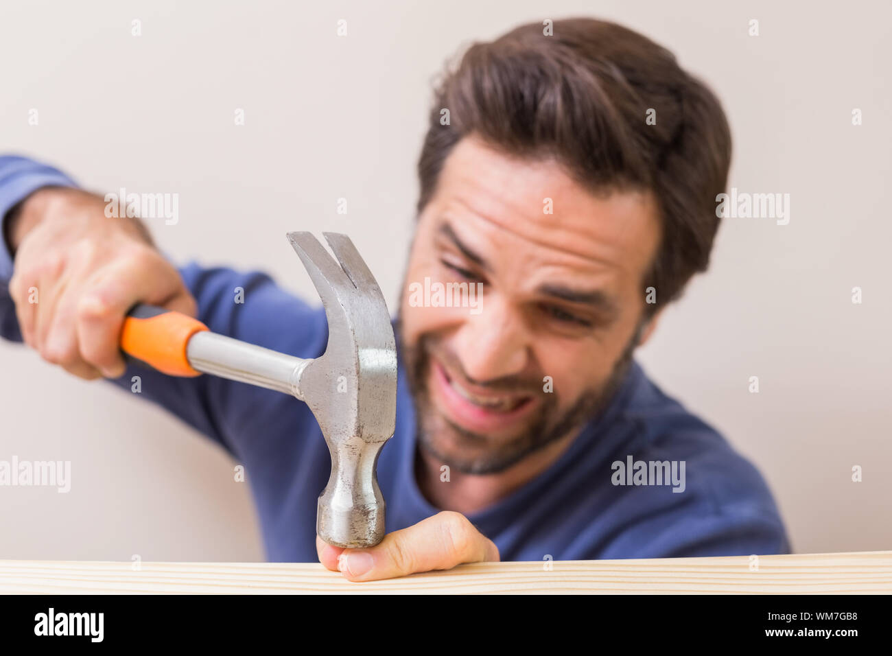 Casual man hammering his finger by accident at home in the living room Stock Photo