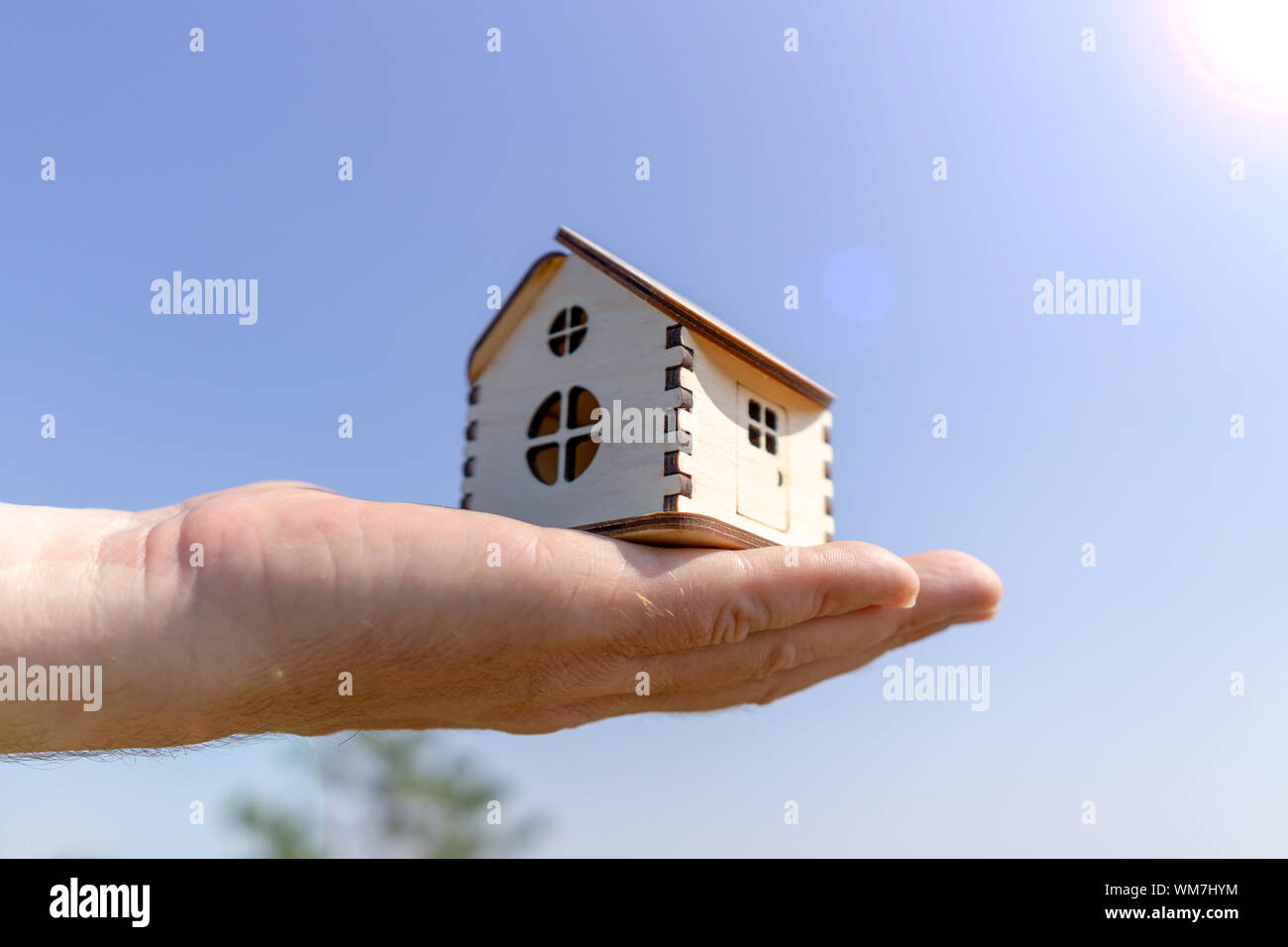 Man holds out a small wooden house in the palm of his hand. Close-up ...