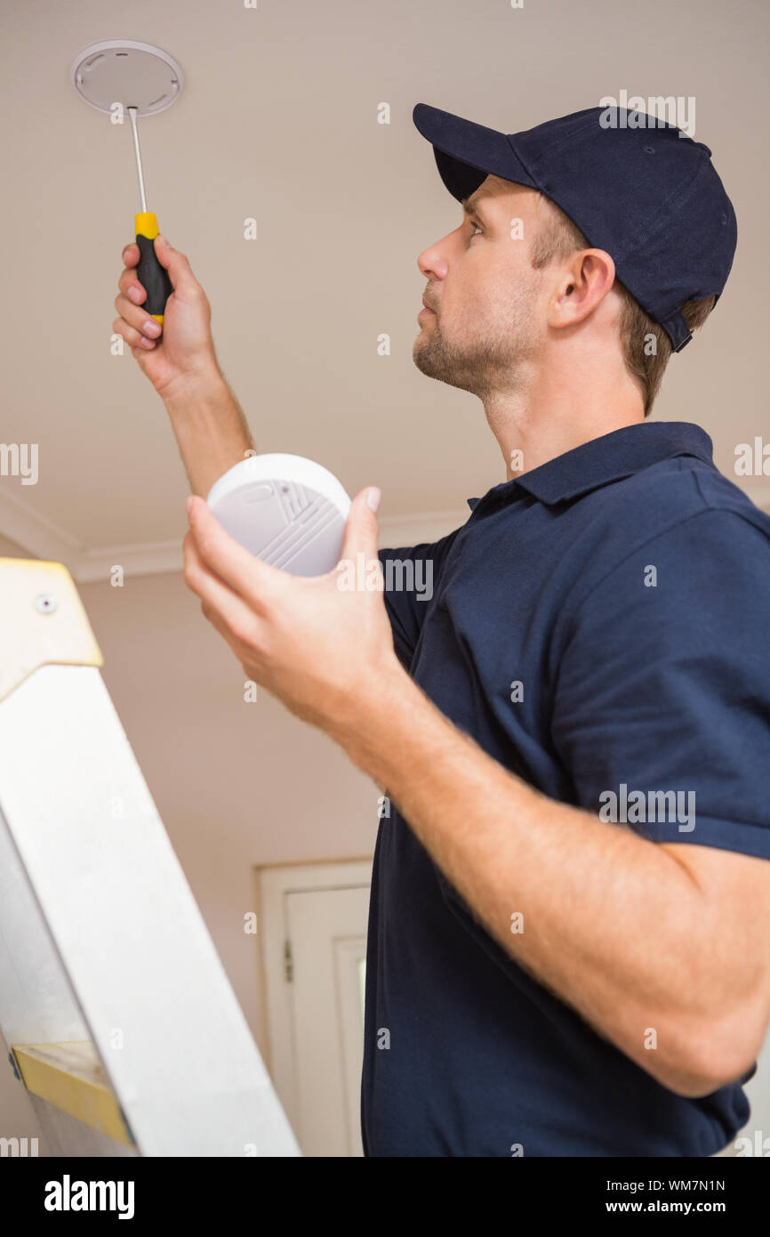 Handyman installing smoke detector with screwdriver on the ceiling Stock Photo