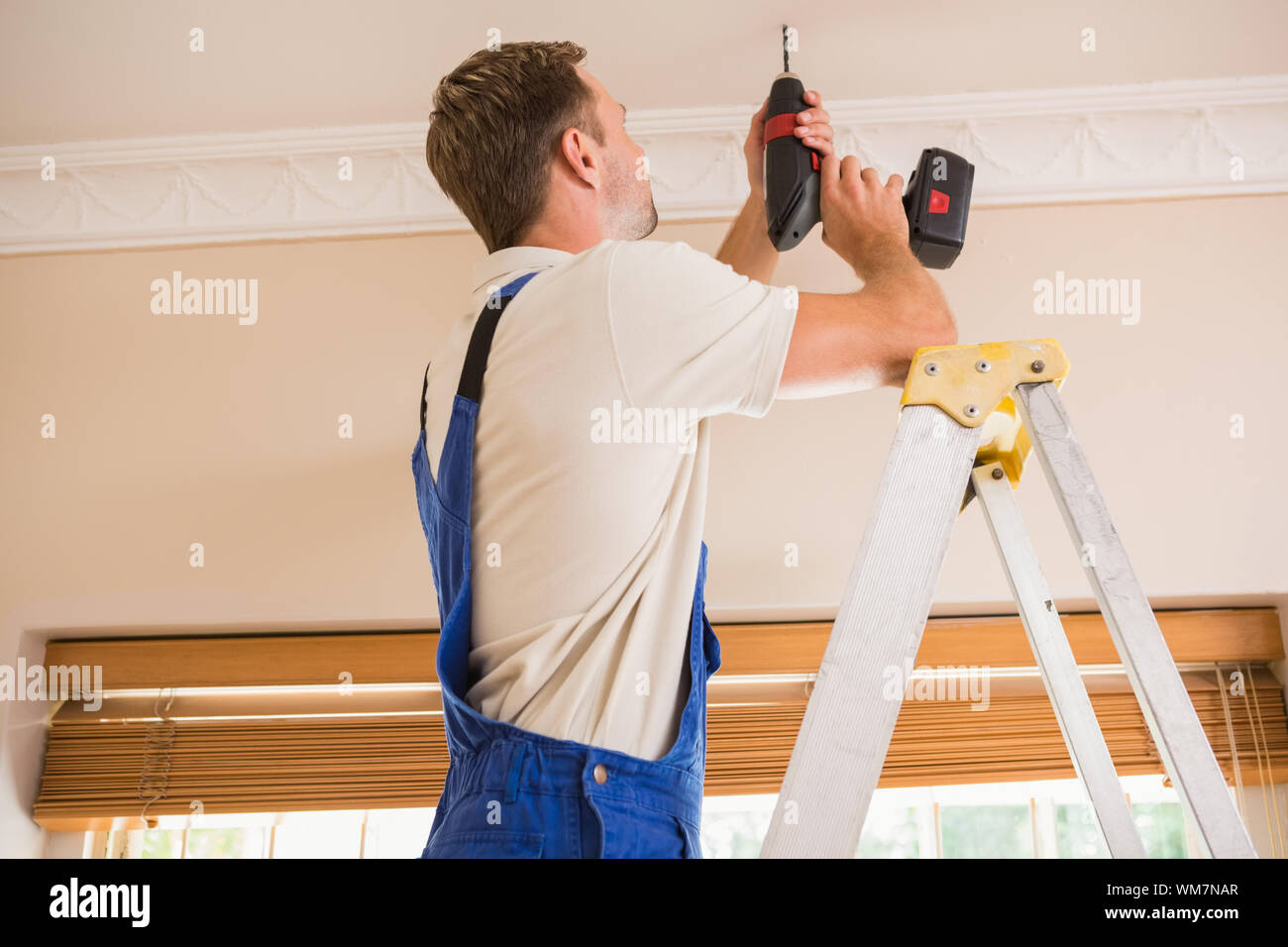 Handyman using a cordless drill to the ceiling in a new house Stock Photo