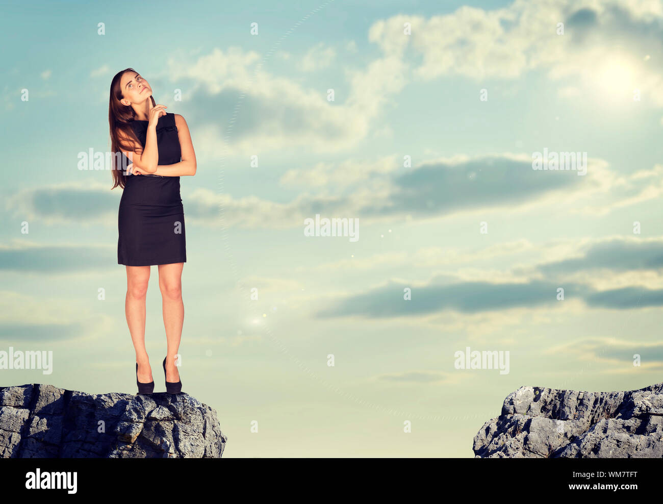 Businesswoman standing on the edge of rock gap in thoughtful pose. Sky ...