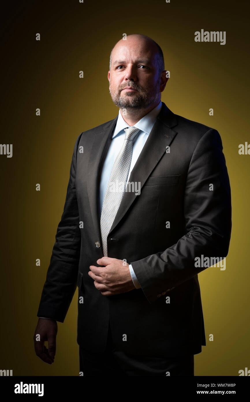 Serious businessman in dark suit and tie against yellow background ...