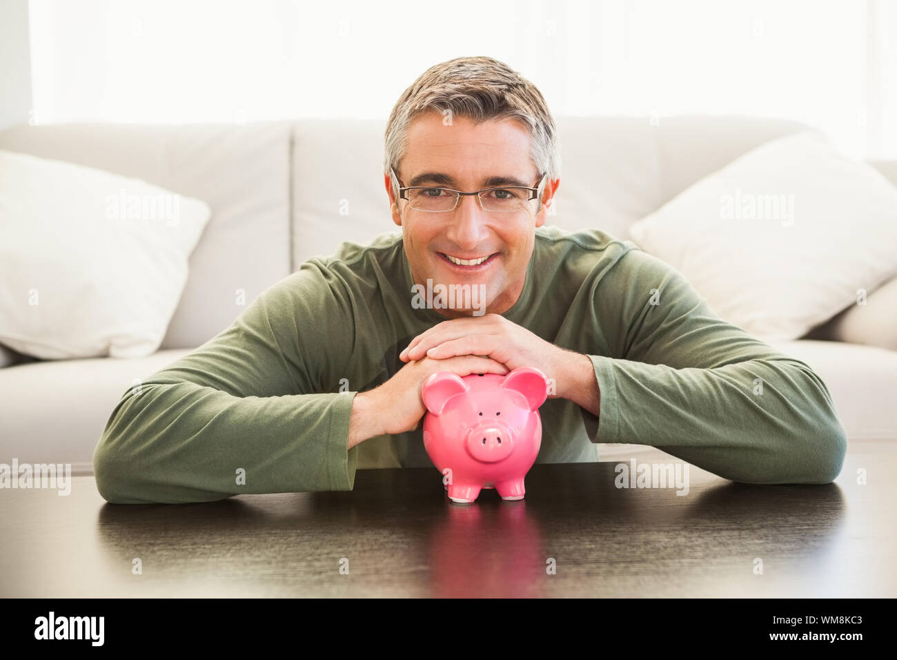 Smiling man with a pink piggy bank at home in the living room Stock ...