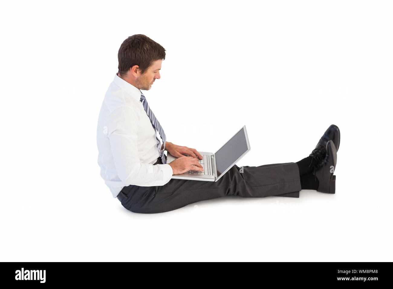 Businessman sitting on the floor typing on his laptop on white ...