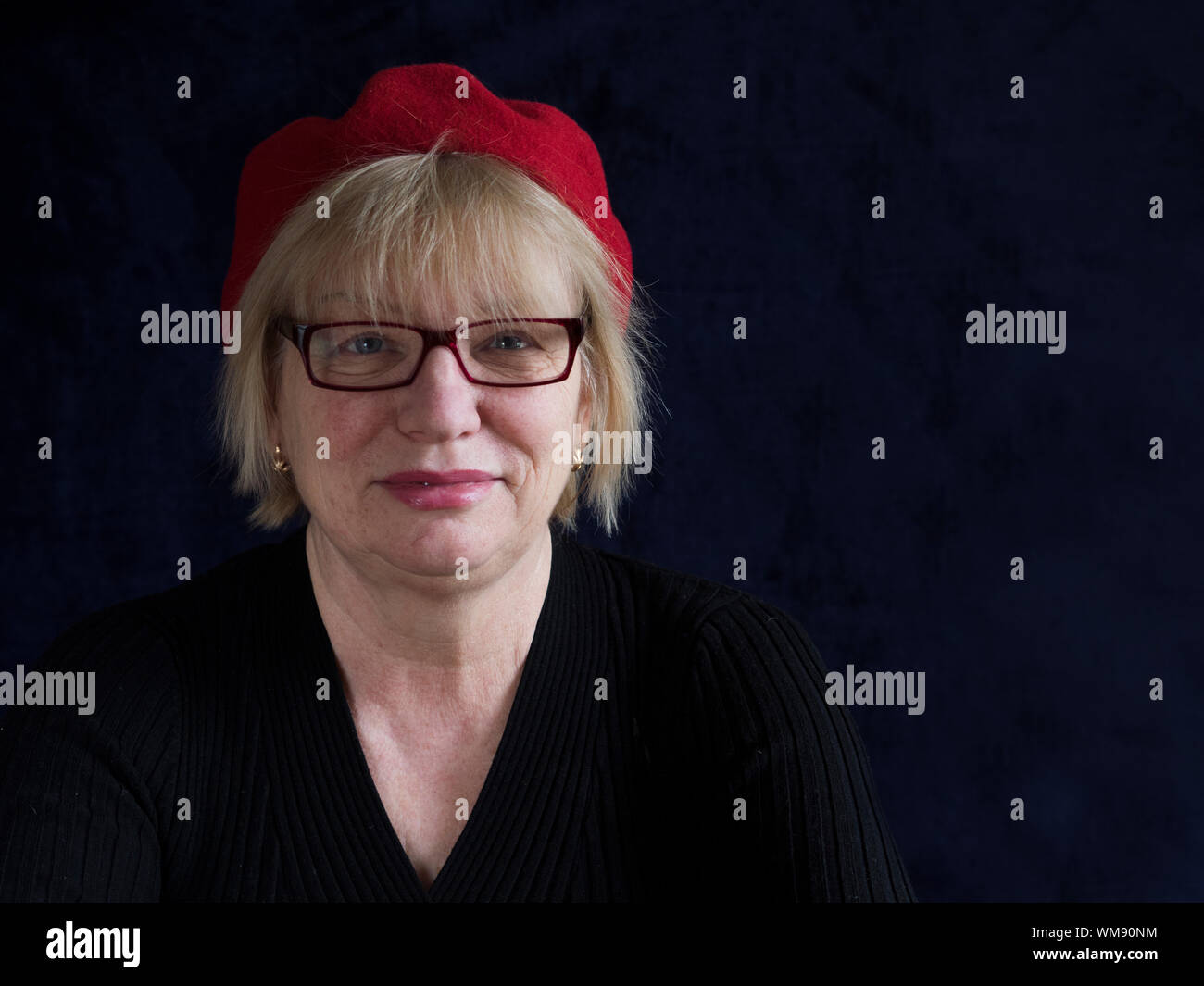 Portrait Of Smiling Mature Woman With Red Cap Against Black Background Stock Photo