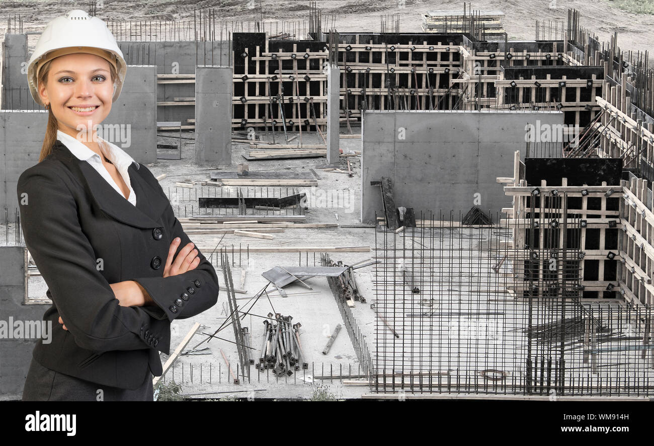 Beautiful businesswoman in suit and helmet standing with crossed arms. Construction site in background. Building concept Stock Photo