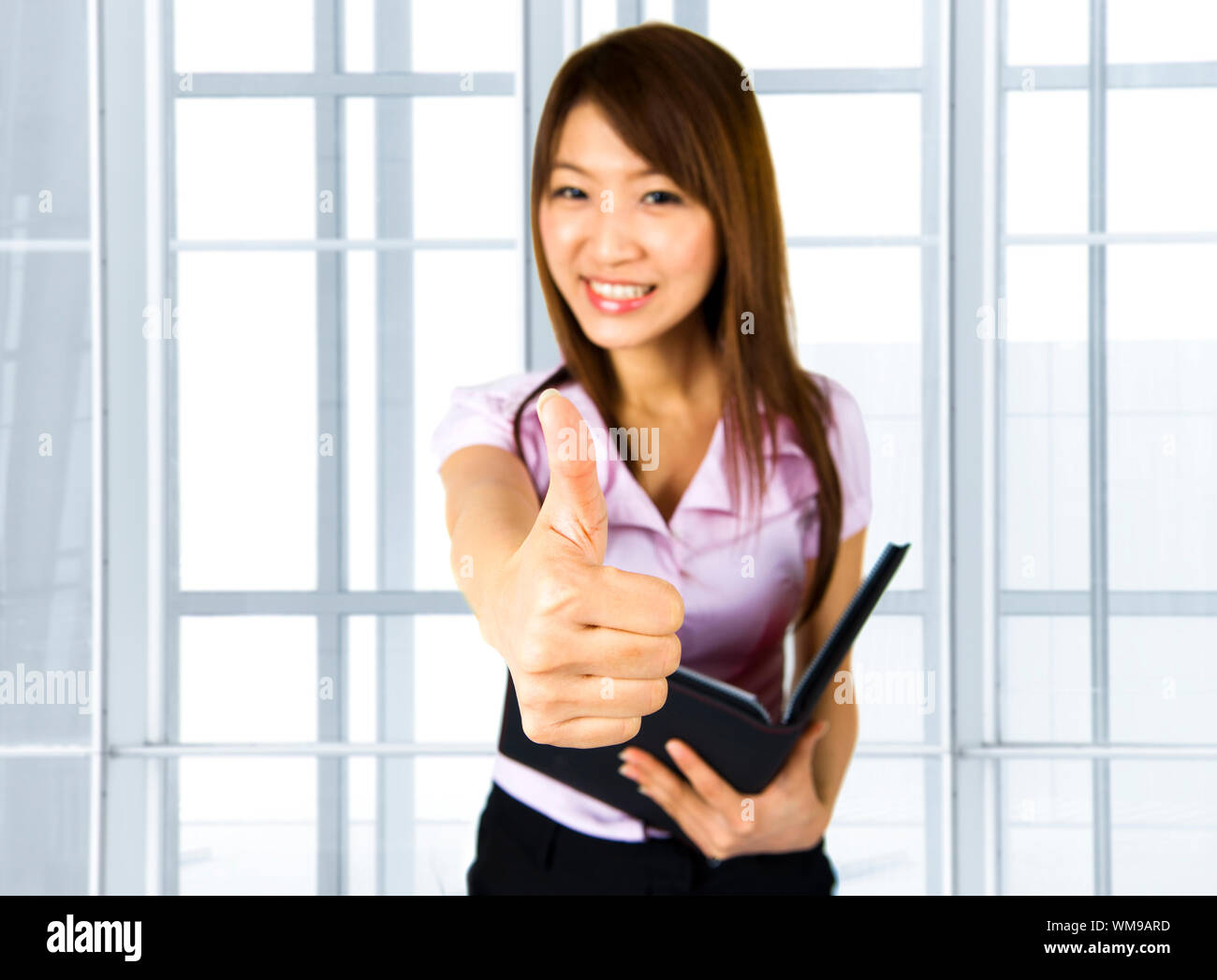 An Asian Girl Giving Thumbs Up Sign And Holding A File In Office