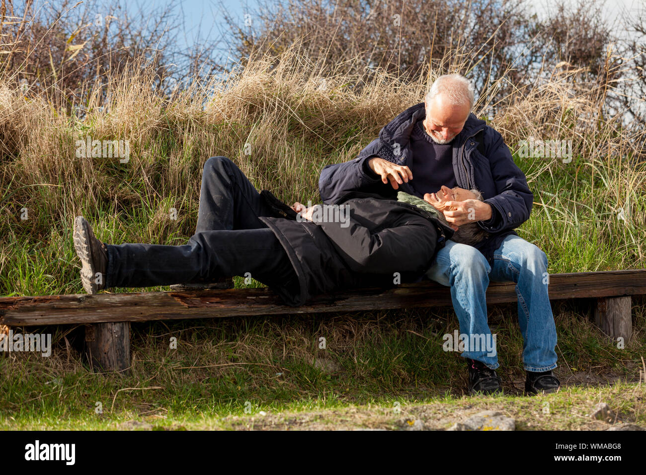 Happy Senior Couple Relaxing Together In The Sunshine On A Wooden