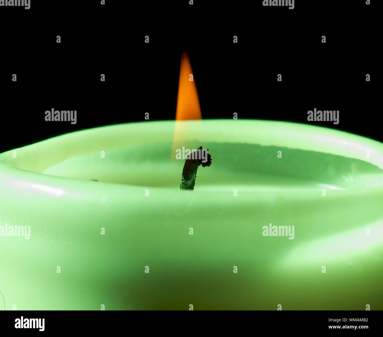 Big Green Candle Burning with Yellow Flame closeup on Black Background