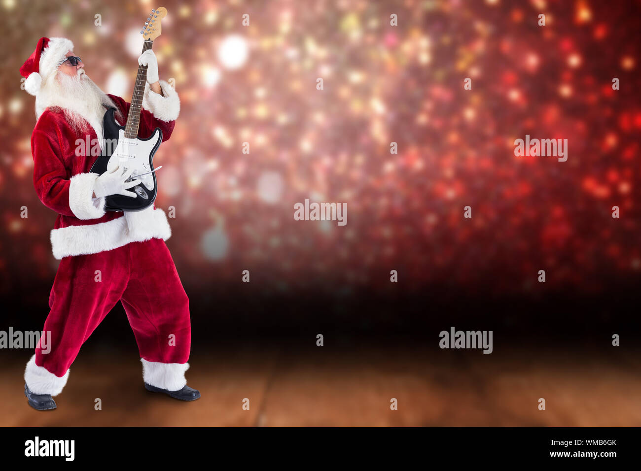 Santa playing electric guitar against shimmering light design over boards Stock Photo