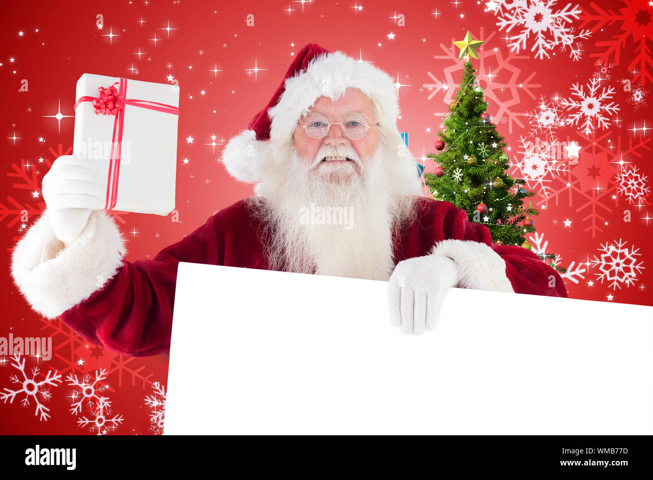 Santa shows a present while holding sign against christmas tree with ...