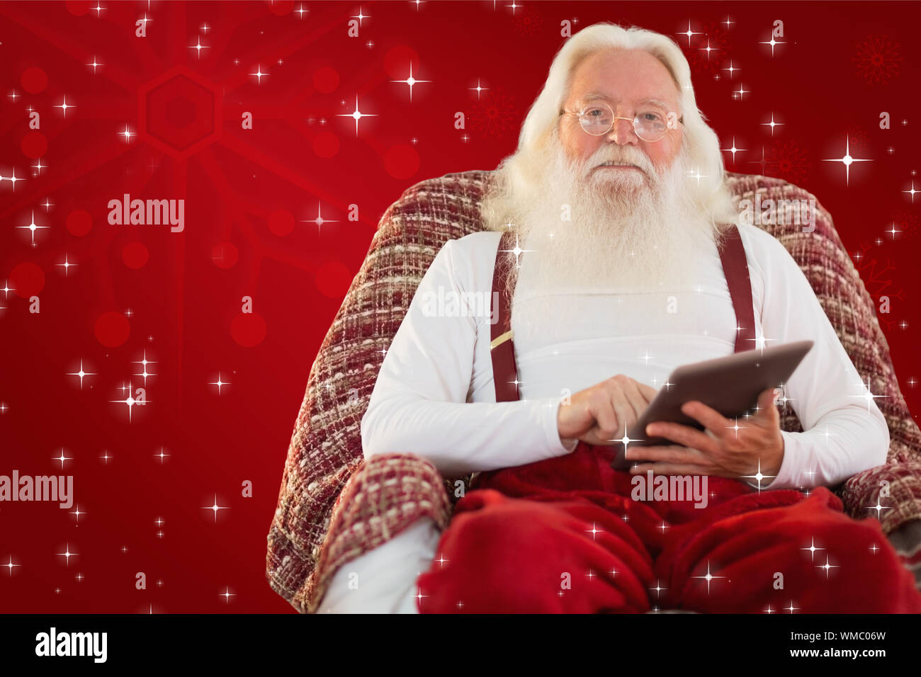 Smiling santa using tablet on the armchair against red background Stock ...