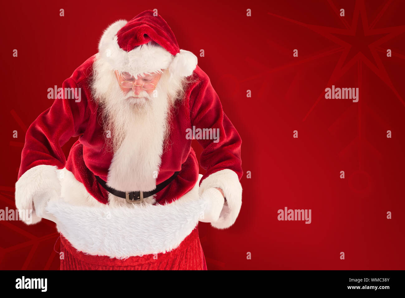 Santa looks in his bag against red background Stock Photo - Alamy