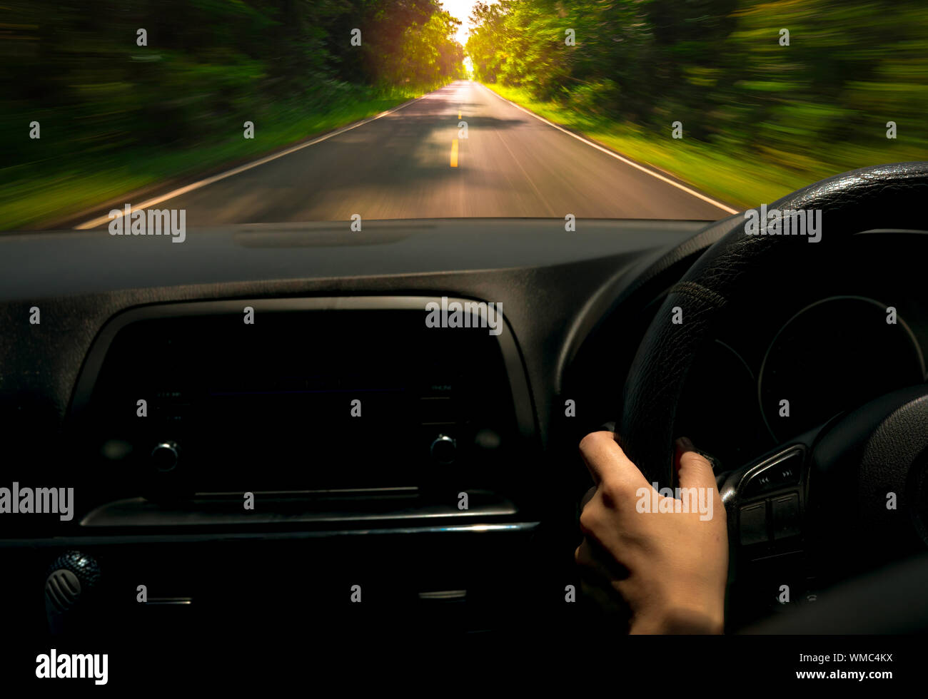 Driver hand holding steering wheel for control car. Inside view of car. Dashboard and windshield. Driving car on asphalt road with motion blur Stock Photo