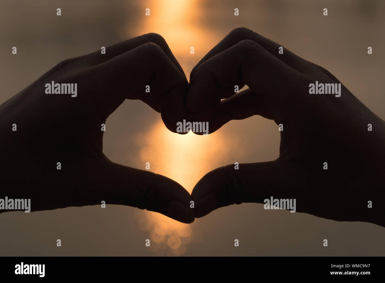 Close-up Of Hands Forming Heart Shape Against Blurred Water Stock Photo