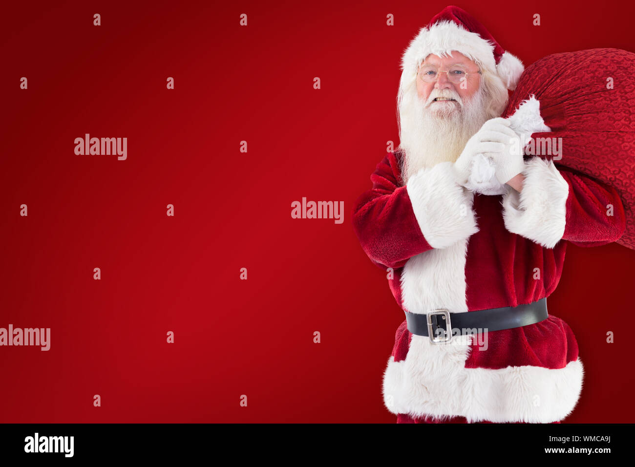 Santa carries his red bag and smiles against red background Stock Photo ...